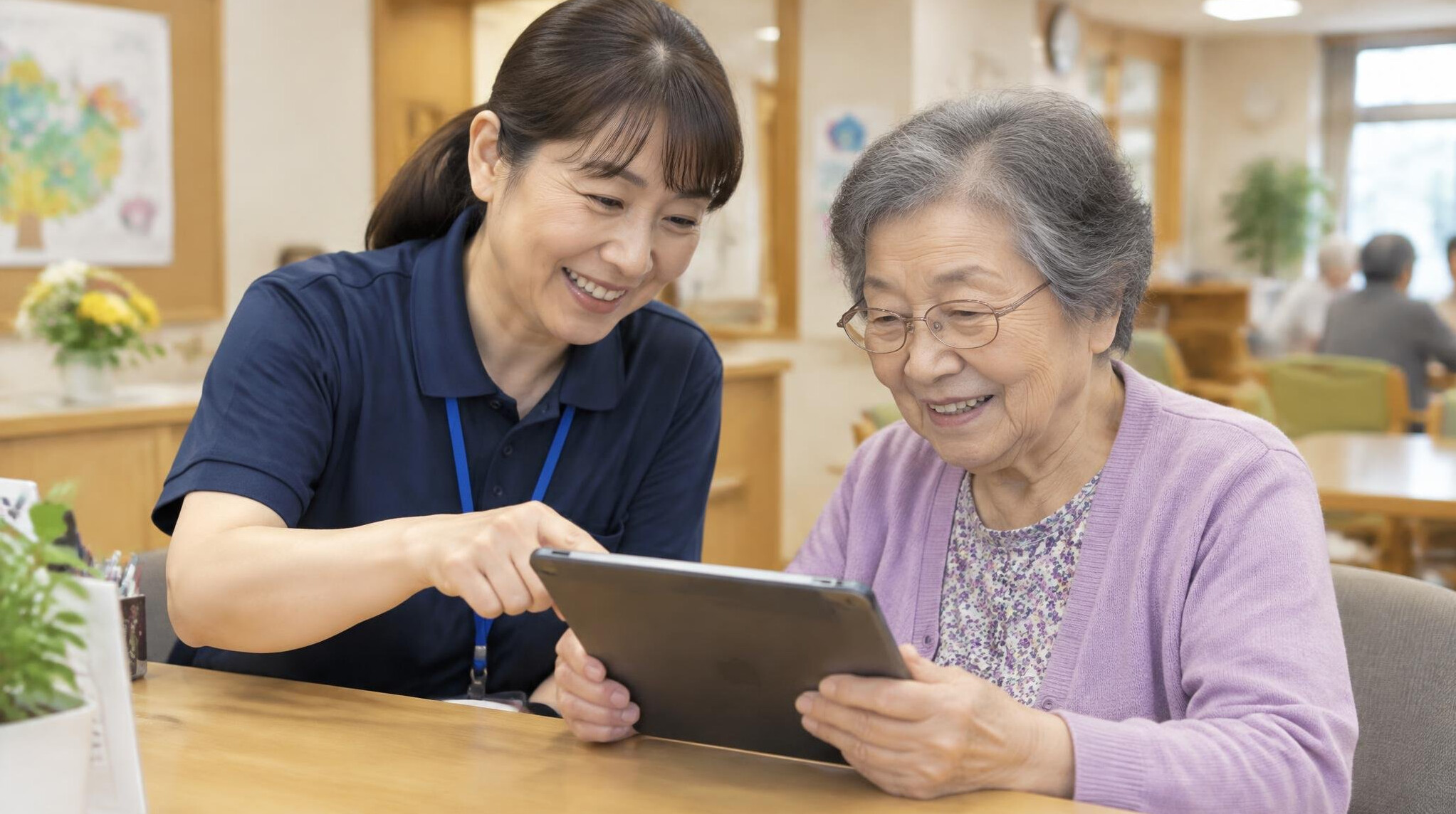 Staff member helping a Japanese senior with a tablet at a reception desk