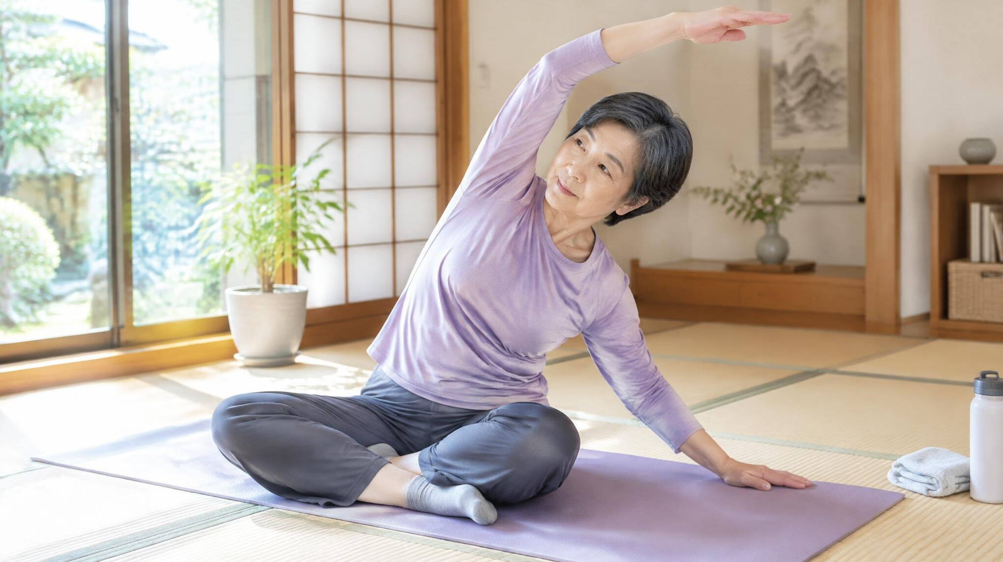 Elderly Japanese woman doing gentle stretching exercise at home